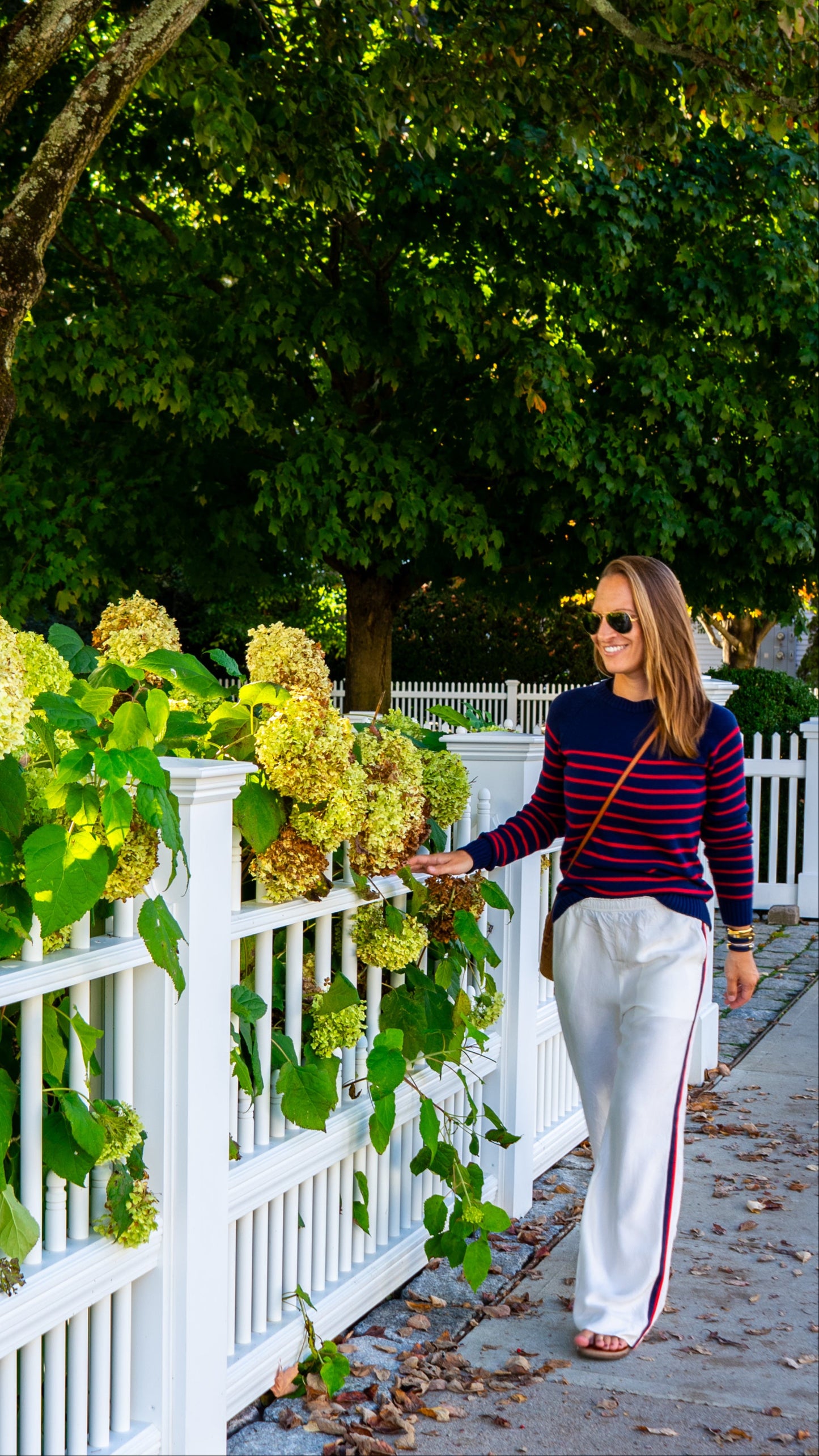 Woman walking along a path lined with greenery and a white picket fence.