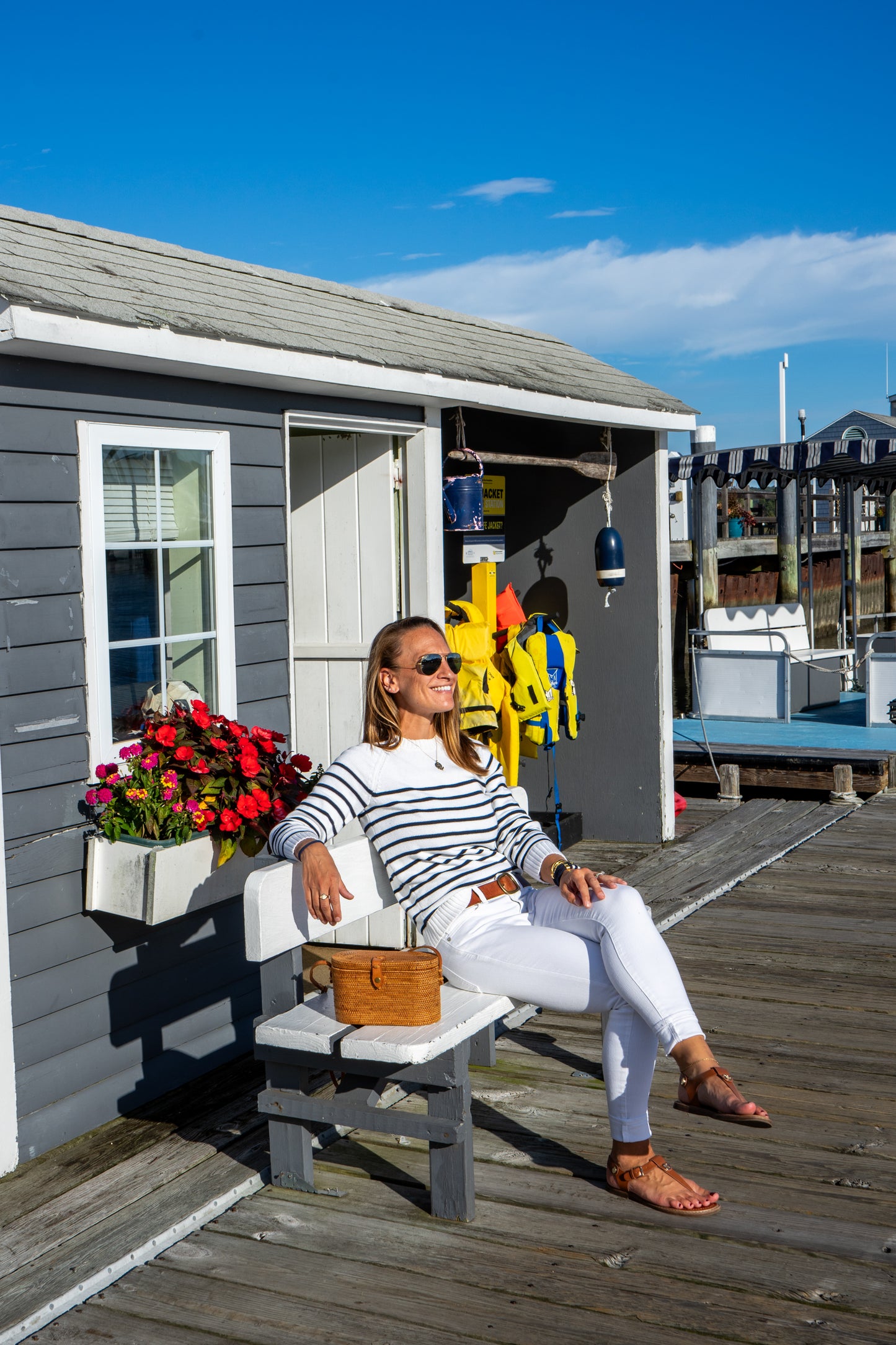Woman sitting on a chair outside a small building with a blue sky and dock in the background